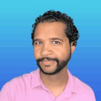 A man with short curly hair and a beard wearing a pink shirt poses in front of a blue gradient background.