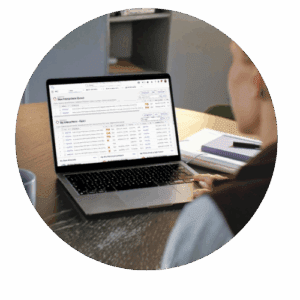 Person working at a desk on a laptop displaying data tables and charts, with a coffee mug and notebook nearby.