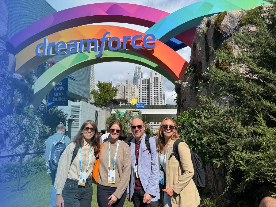 Four people stand and smile under a colorful arch that says “dreamforce” at an outdoor event, with buildings and greenery in the background.