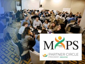 A large group of people sit at round tables in a conference room, engaging in discussion. In the foreground is a MAPS Partner Circle Program Executive logo.