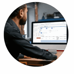 A person sits at a desk and works on a computer displaying a software application with tables and charts.