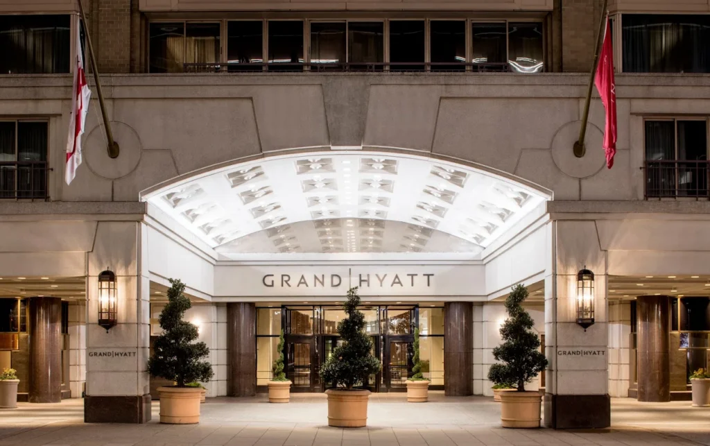 Grand Hyatt hotel entrance at night, featuring illuminated canopy, glass doors, potted plants, and two flags on either side of the entrance.