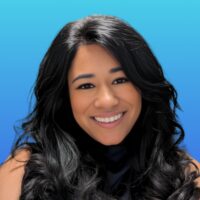 Smiling woman with long black hair, wearing a dark top, posed in front of a blue gradient background.