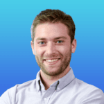 A man with short brown hair and a beard, wearing a light blue button-up shirt, smiles in front of a blue gradient background.