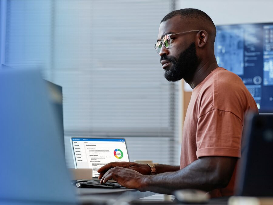 Man wearing glasses working at a desk, looking at a computer screen displaying a dashboard with a colored chart and data.
