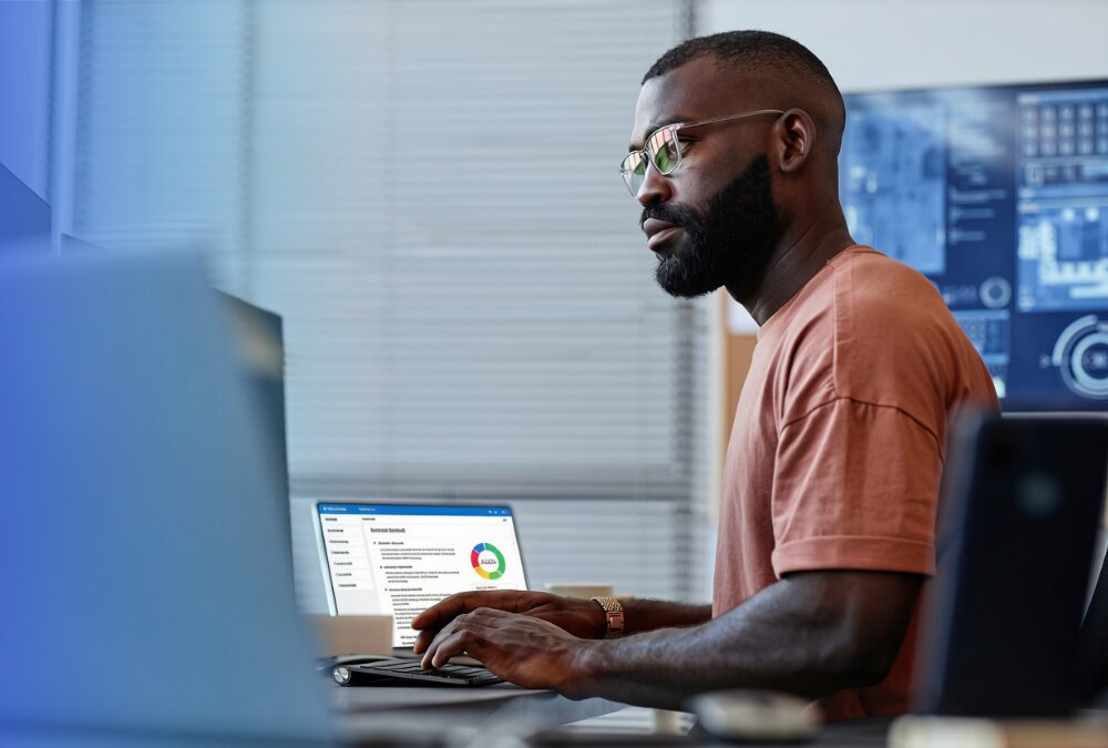 Man wearing glasses working at a desk, looking at a computer screen displaying a dashboard with a colored chart and data.