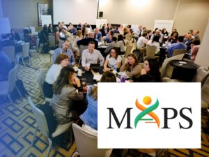A large group of people seated at round tables in a conference room, with the MAPS logo overlaid in the foreground.